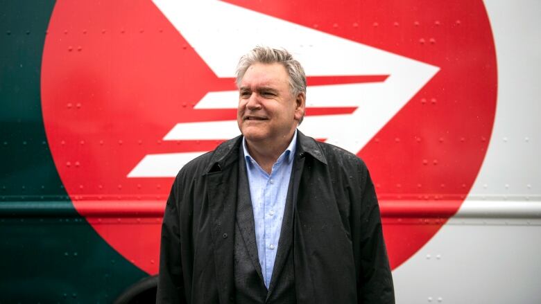 A man stands in front of a red and white truck that bears the Canada Post symbol.