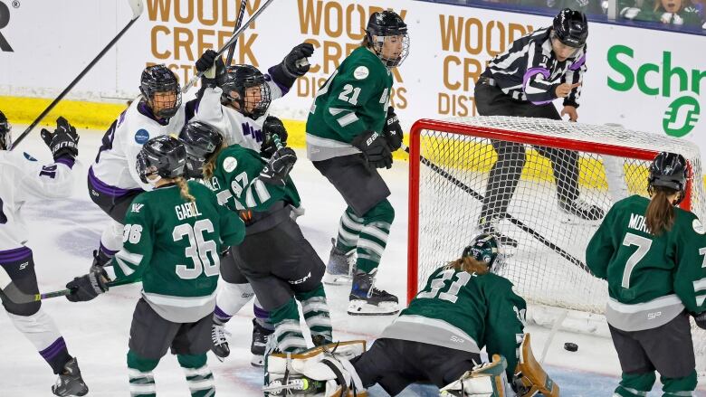 A women's hockey player raises her arms in celebration after scoring a goal.