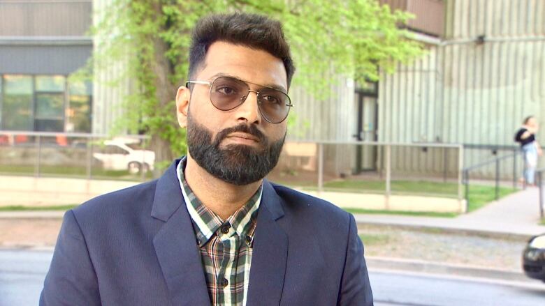 A man standing on the street behind a green building wearing a navy sport coat.