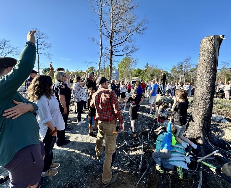 A crowd of people stand on a gravel trail, some with their hands raised.