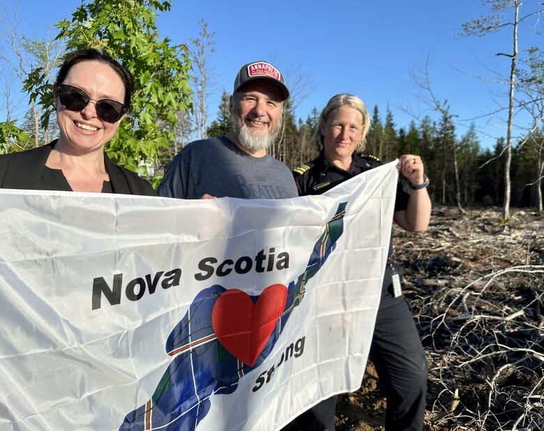 Three people hold up a flag that says Nova Scotia Strong.