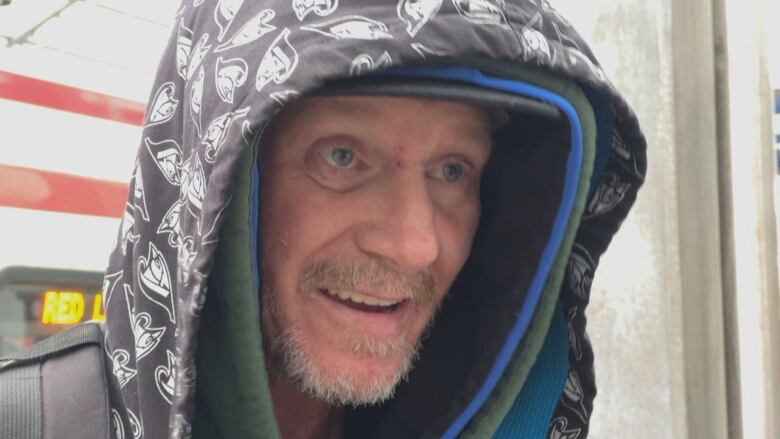 A man wearing a hood smiles at the camera.