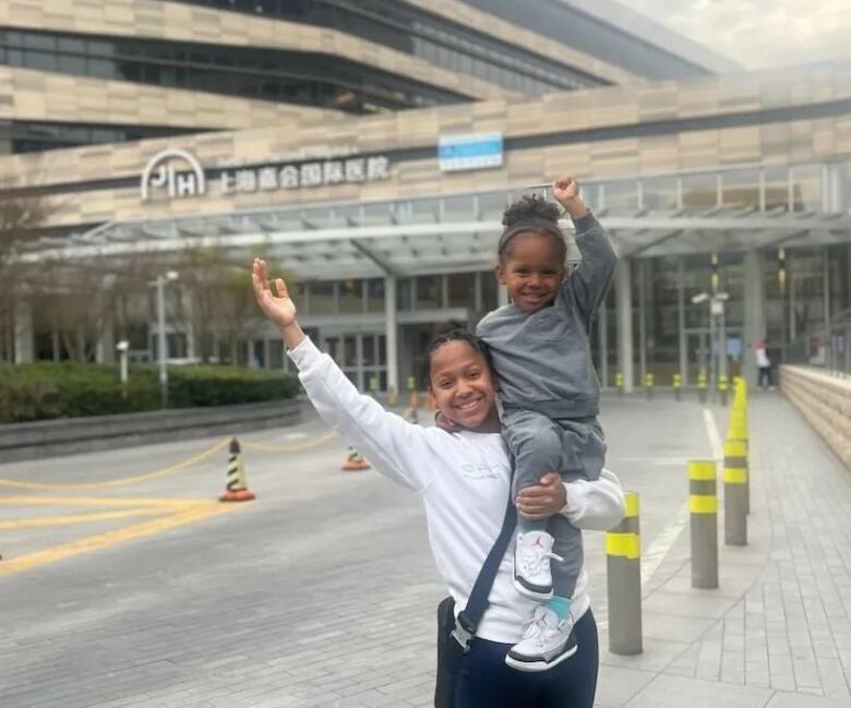 A big sister holds her younger brother outside of a hospital. They smile for the photo.