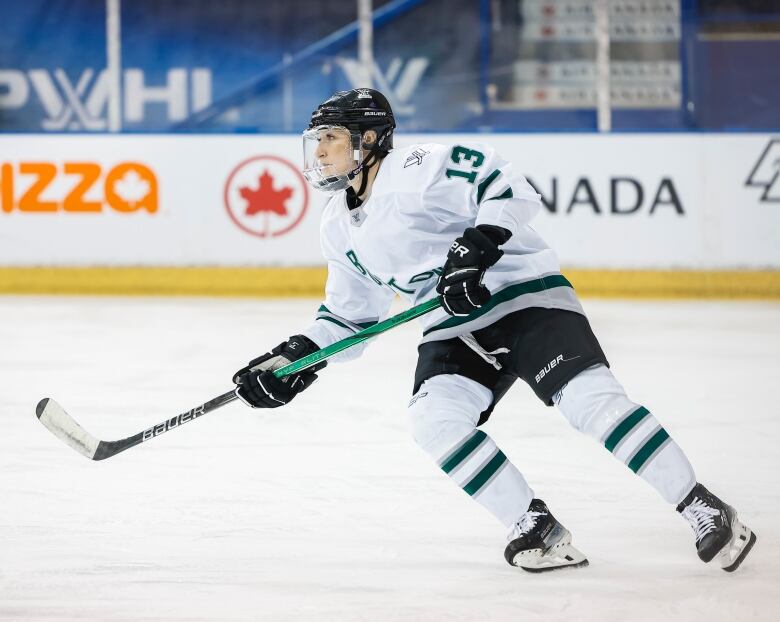 A woman in a team hockey jersey with her hockey stick in front of her flies down the rink.