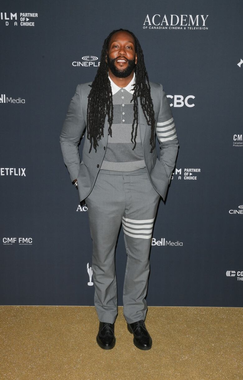 Tyrone Edwards on the Canadian Screen Awards red carpet wearing a grey and white suit and a polo shirt.  