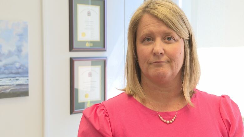 Woman with shoulder-length blonde hair wearing a pink dress and pearls in an office.