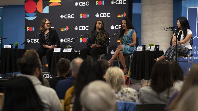 Jane Philpott, Amie Archibald-Varley, Sheila Singh and Sara Fung sitting in row, watched by a crowd.