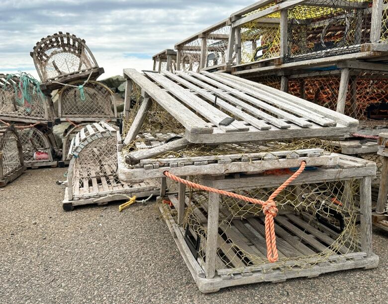 Several wooden lobster traps stacked on a wharf, some with the wood frame smashed, others with the mesh cut open.