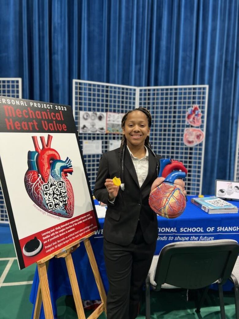 A young woman holds a model heart, next to a sign that says, mechanical heart valve.