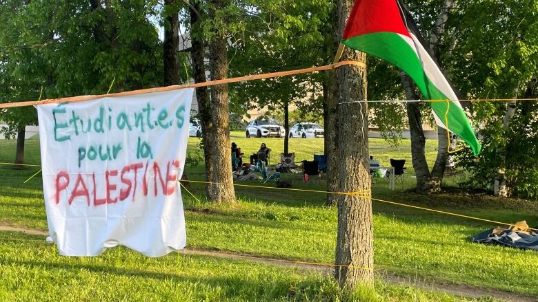 A sign reading Etudiantes pour la Palestine hung up in a grassy area between trees. 