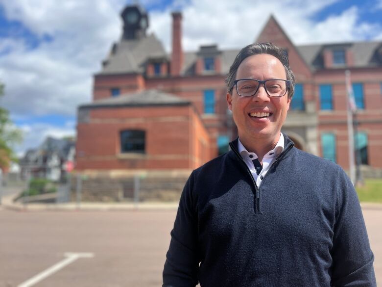 Kutcher is wearing glasses and a blue sweater as he stands before Summerside's city hall and the brick portion slated for demolition.