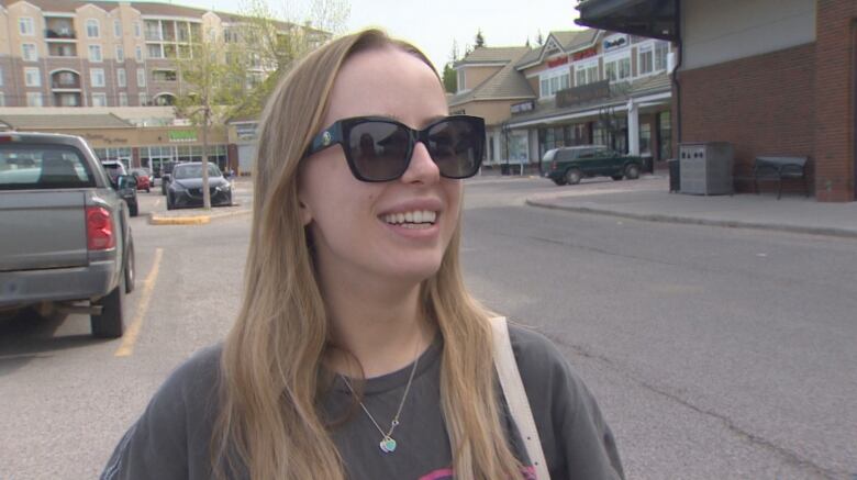 A woman with blonde hair and sunglasses is smiling in a parkade.