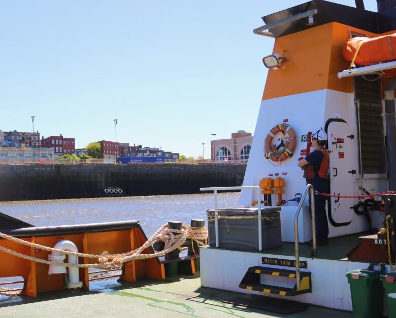 A man in a helmet and life jacket looks out over the brick homes and cruise terminals of along the port of Saint John. 