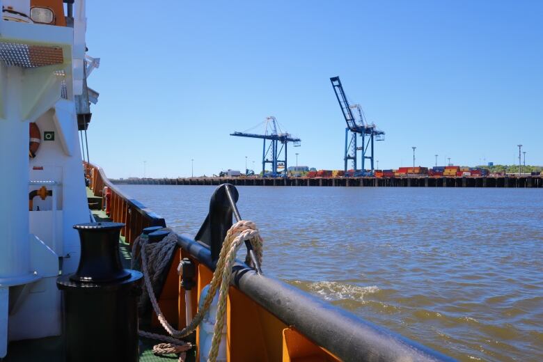 Blue cranes and brightly-coloured shipping containers viewed from the water in the harbour of Saint John. 