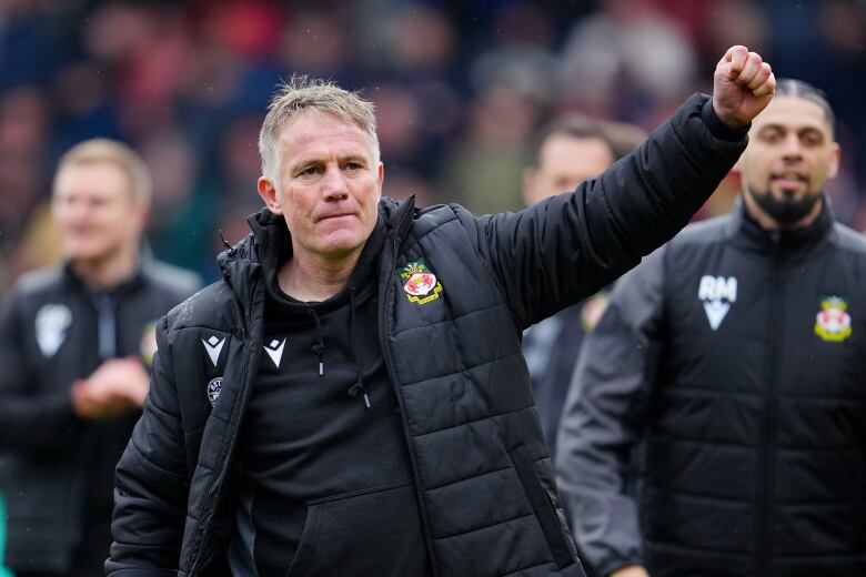 Men wearing football jackets celebrate on the pitch, with one man in the centre raising his arm.