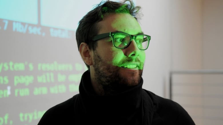 A middle aged man talking. His face is lite with the green glow of a projector.