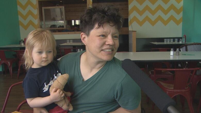 Steph McNair holding their daughter Maeve while speaking into a microphone.