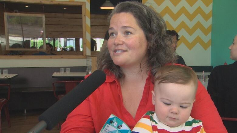 Kelly Manning holding her daughter Catherine while speaking into a microphone.