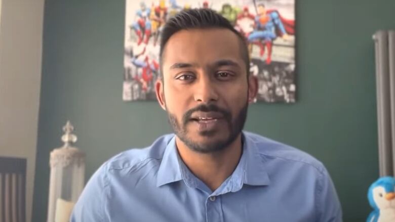 A man in a blue collared shirt is seen looking forward.