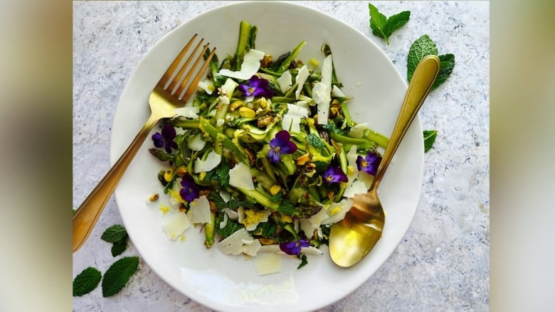 An artfully framed photo of a salad with shaved asparagus, bits of cheese and a few other herbs.