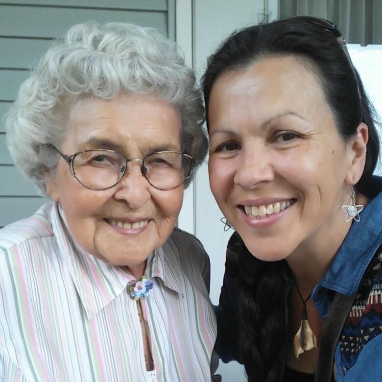 A white-haired older woman and her adult granddaughter smile as they pose together. 