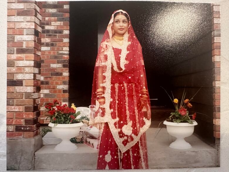 A bride in a red Indian wedding sari stands in front of a fireplace.