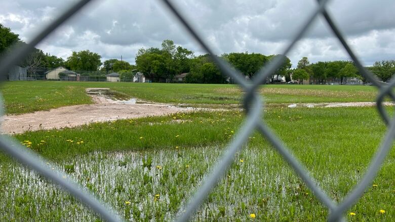 A baseball field can be seen through a chain link fence. The field is saturated in water. 