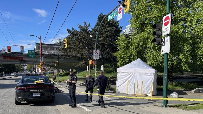 A white tent is shown with yellow police tape and a police car with three officers.