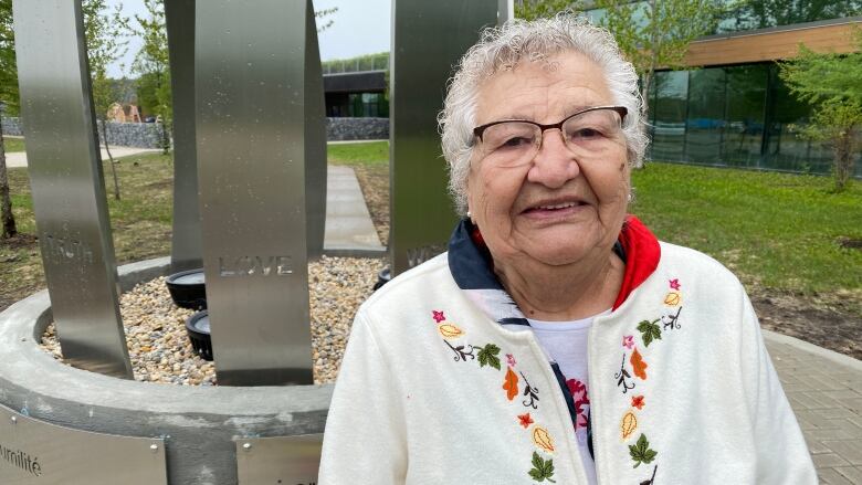 An elder stands in front of a sculpture on a rainy day.