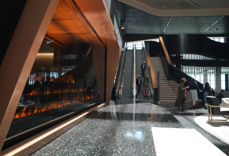 Two escalators and a set of stairs lead up to a higher level in a massive venue. A wall shows decorative flames beside the escalators.