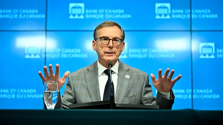 A man speaks into a microphone and gestures with his hands during a news conference.