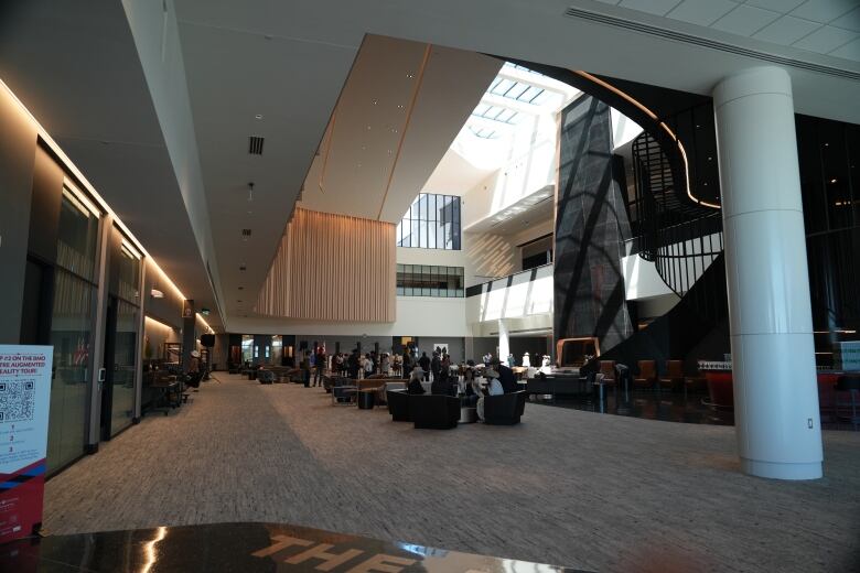 A venue corridor is carpeted with chairs and tables on the ground floor. Natural light shines through big glass windows.