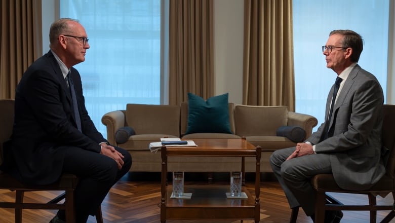 Two men are shown seated opposite each other with a coffee table between them.