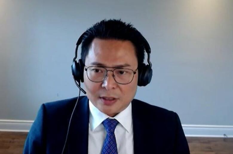 A man in a blue suit and tie speaks into a headset.