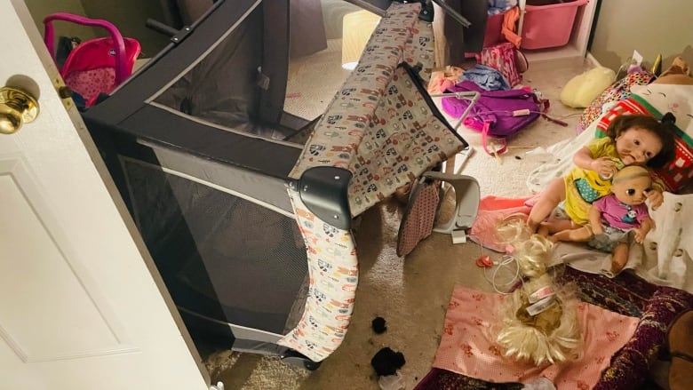 A messy room shows a crib knocked over, dolls and other items on the ground.