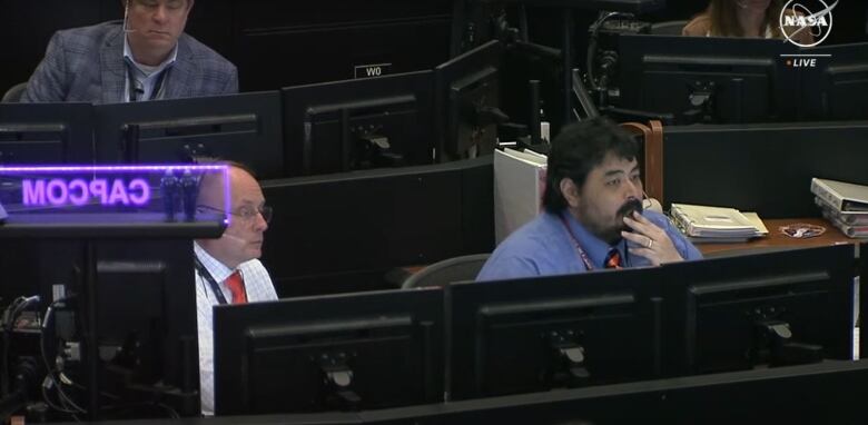 Two men behind several computers look serious.