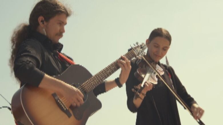 A man plays guitar and a woman plays a fiddle