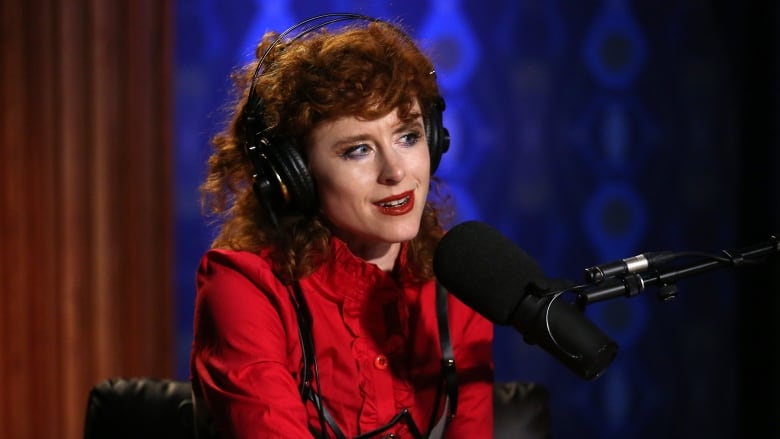 Headshot of Kiesza wearing a red shirt and over-ear headphones with a studio microphone in front of her.