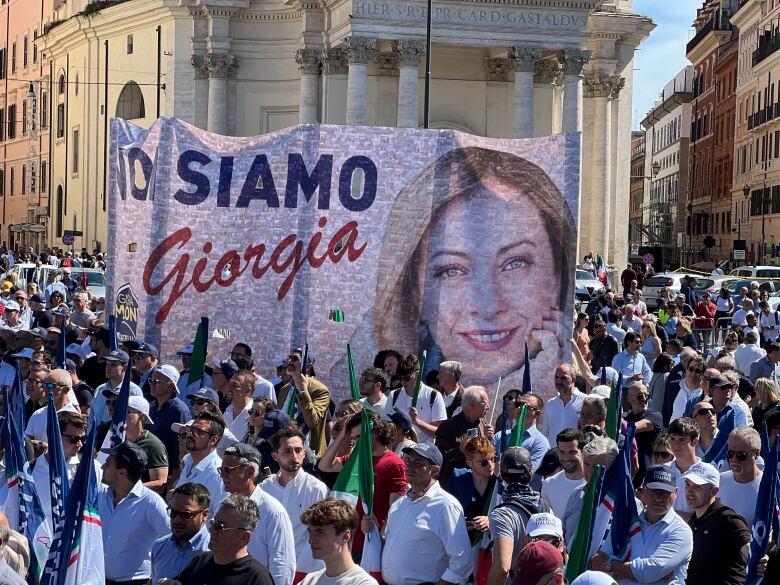 A crowd gathers as some among them carry a large poster with the picture of a person on it and the word 'Giorgia.'