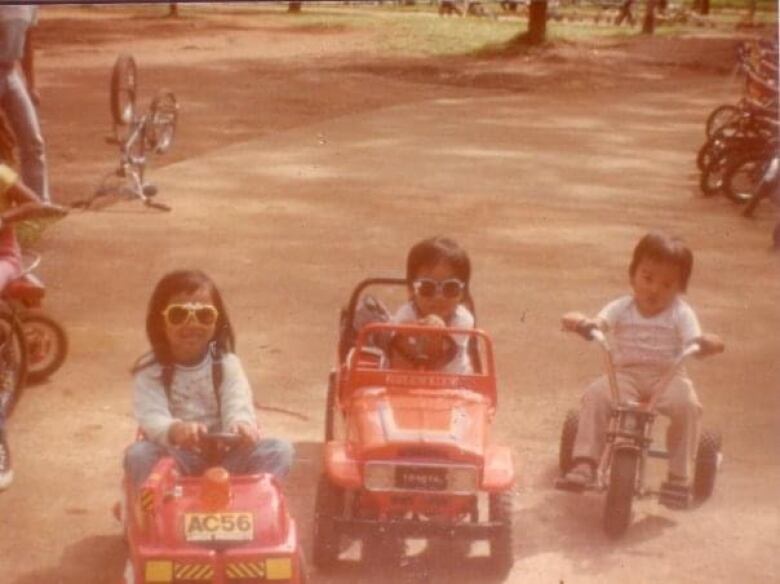 Three kids on kiddie cars and a bicycle