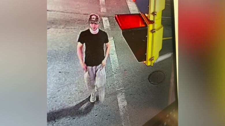 man wears black hat, black t-shirt, grey sweat pants and sneakers as he crosses the street