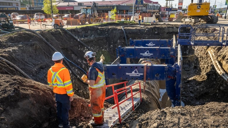 Two workmen stand next to an exposed section of water main pipe.