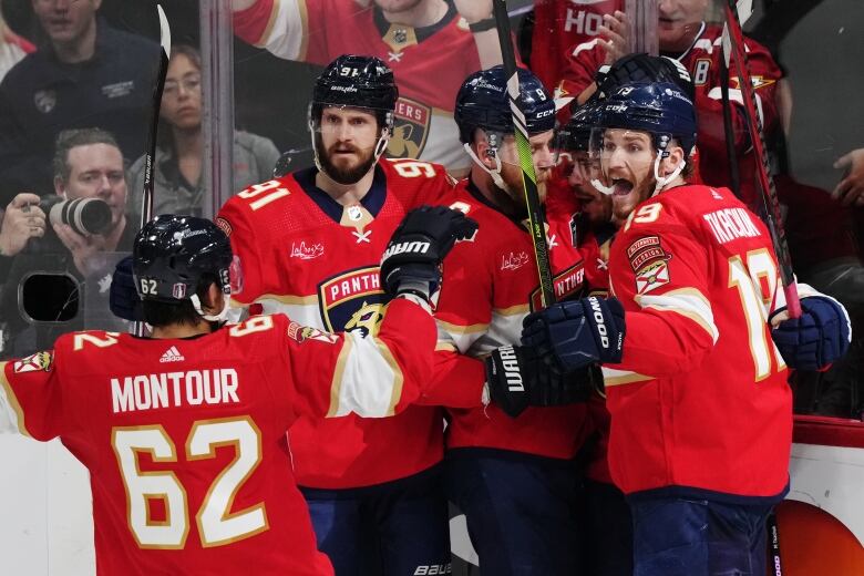 Five male hockey players celebrate a goal near the glass separating the rink from the fans.