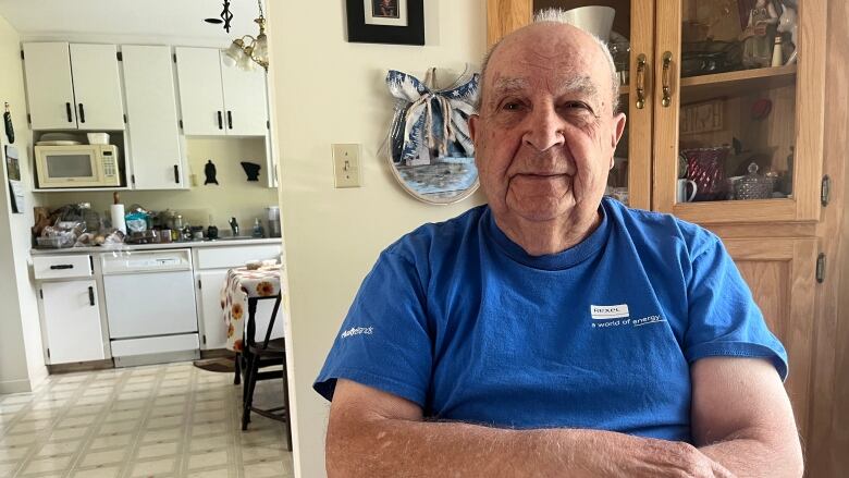 Man with blue shirt sitting at table with kitchen in background.