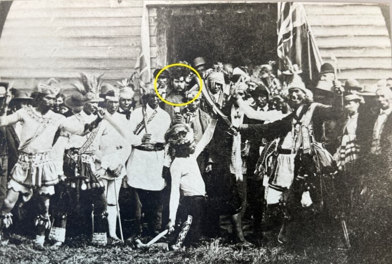 A black and white pictures shows several Six Nations people in ceremonial regalia posing for a picture.