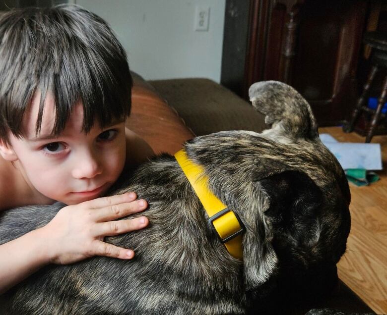 A brown haired child snuggles his dog. The child is looking into the camera.