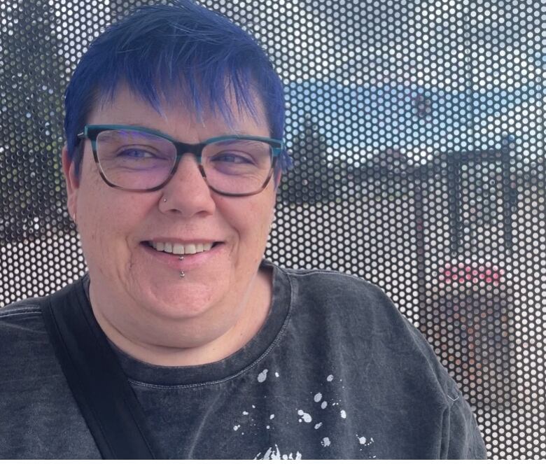 A woman with blue hair and glasses smiles.