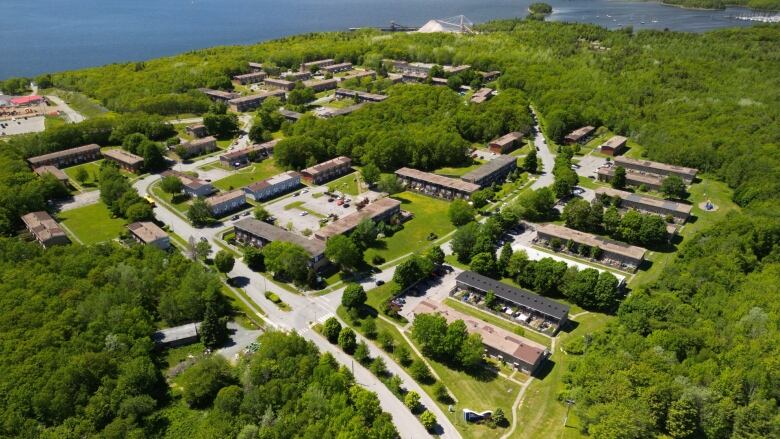 A community of low-rise apartments and townhouses, surrounded by forest and ocean, is seen in an aerial shot.