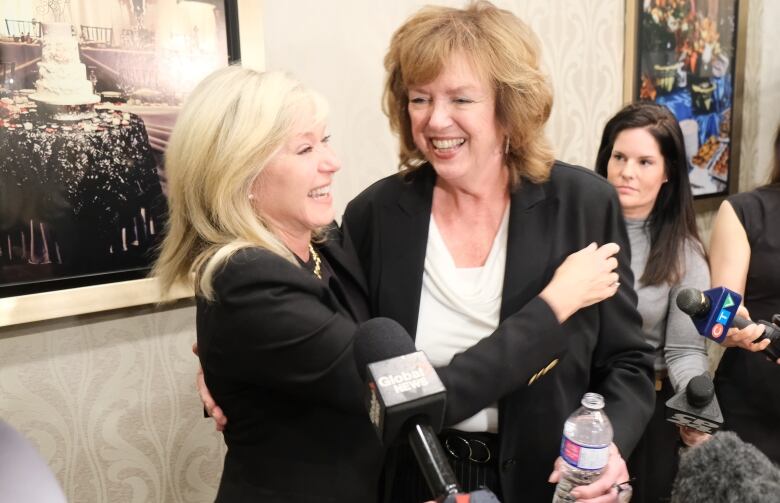 Bonnie Crombie hugs Carolyn Parrish as reporters look on. 