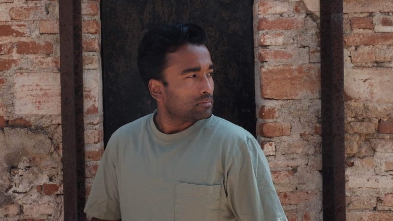 A Brown man with short dark hair looks off camera wearing a pale green t shirt.